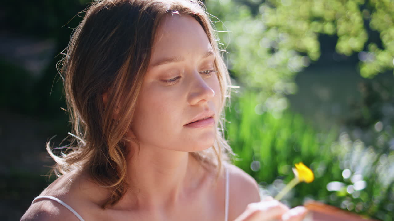 Gentle girl reading book in sunny summer garden closeup. Woman holding flower