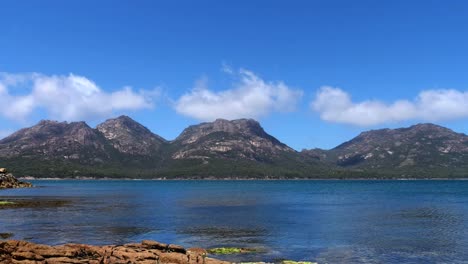 Lapso-De-Tiempo-De-Nubes-Rodando-Sobre-La-Cordillera-Rocosa-En-Un-Día-Soleado-Y-Claro-De-Verano-Con-Goteo-De-Agua-Azul-Del-Océano-En-Primer-Plano,-Freycinet,-Tasmania