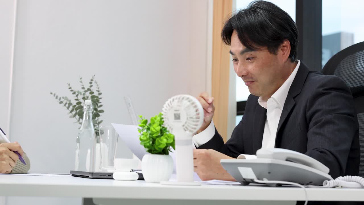 スーツを着たアジア系のビジネスマンが、プロのオフィスでの会議中に書類を確認し、話をしています。
