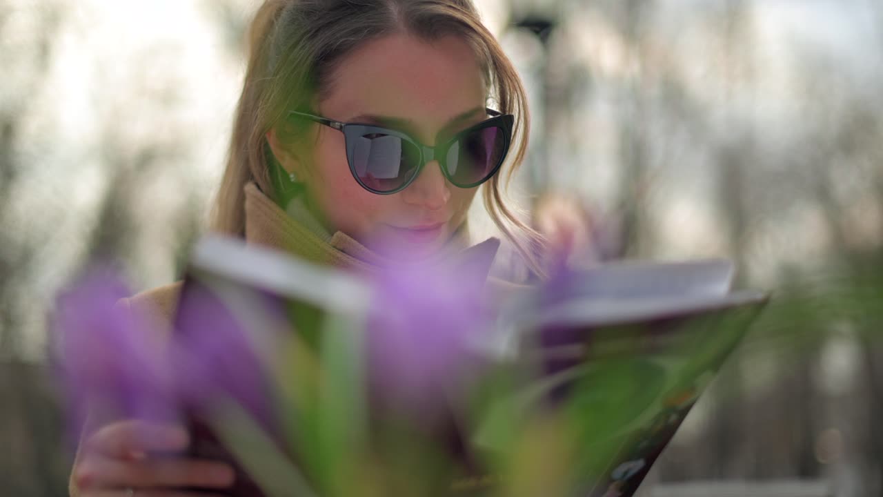 Brunette woman in brown coat reading a book at a terrace