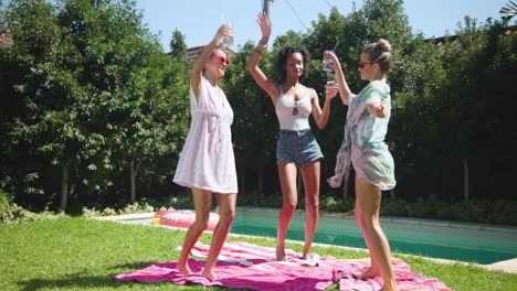 diverse female friends enjoying drinks and dancing by pool on sunny day, wearing sunglasses