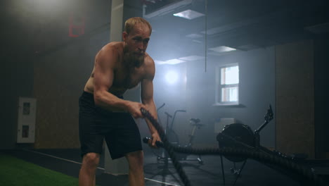 male athlete working out with ropes in old building. athlete man in training with ropes near mirror. battle rope
