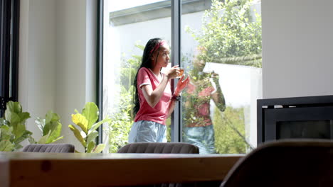 joven afroamericana con un teléfono inteligente, de pie junto a la ventana