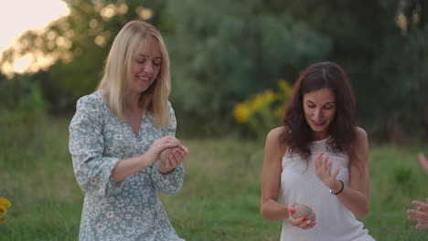 a group of young women sculpts out of clay in nature in a park in an open space. two girls are engaged in close-up modeling smiling talking enjoying the process.