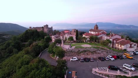 Aerial-reveals-castle-over-looking-historic-village-at-sunset,-Italy