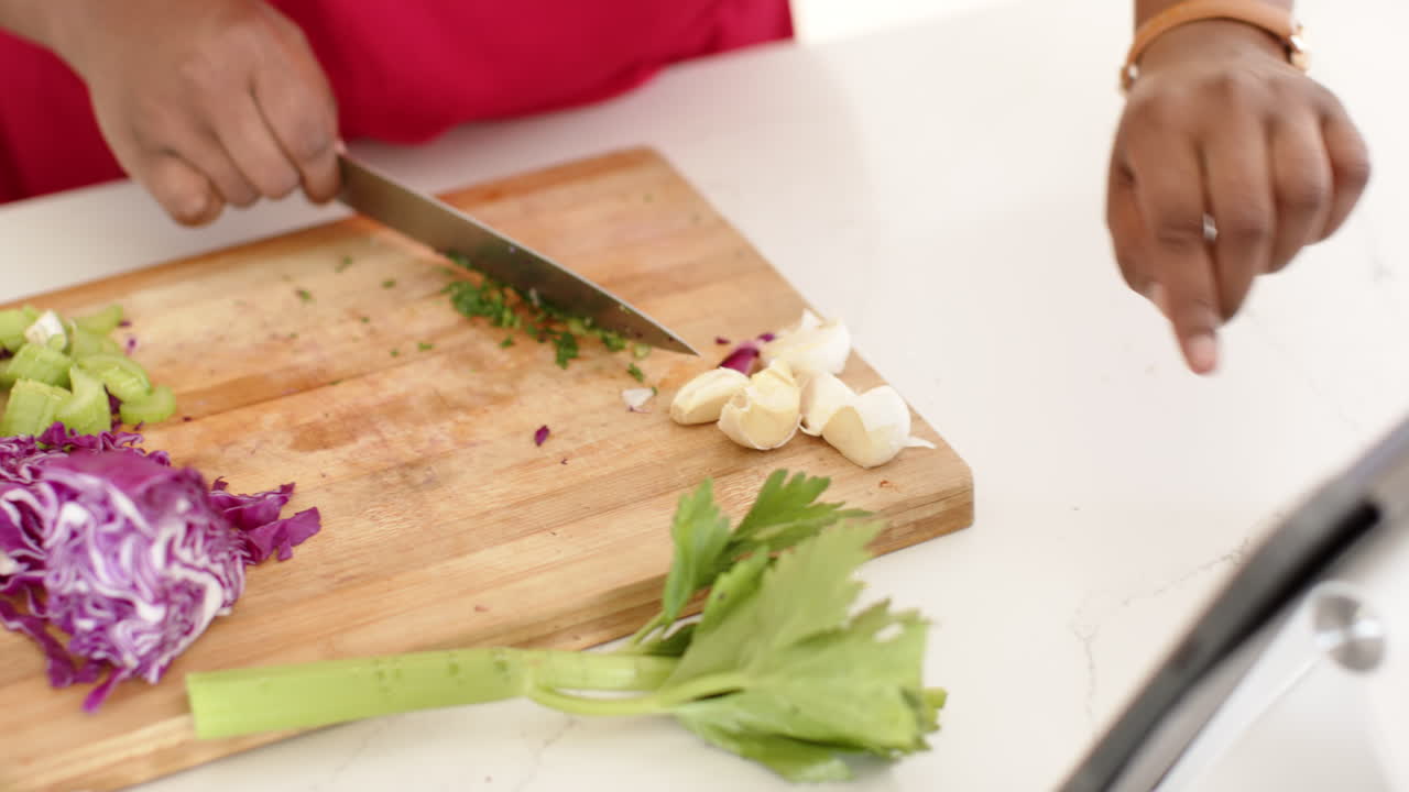 African American woman is finely chopping herbs on a wooden cutting board at home