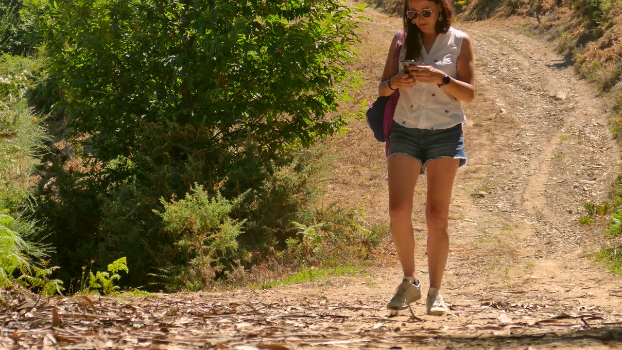 excursionista mujer navegando en el libro electrónico en su teléfono mientras camina bajo el sol