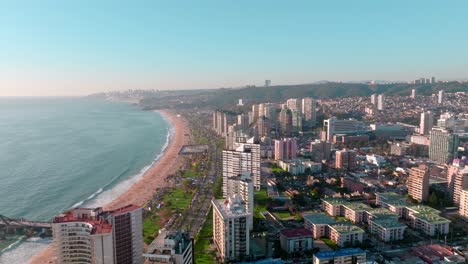 Carretilla-Aérea-De-Los-Edificios-Del-Barrio-De-Viña-Del-Mar-Cerca-De-La-Costa-De-Arena,-Mar-Turquesa-Y-Muelle,-Chile