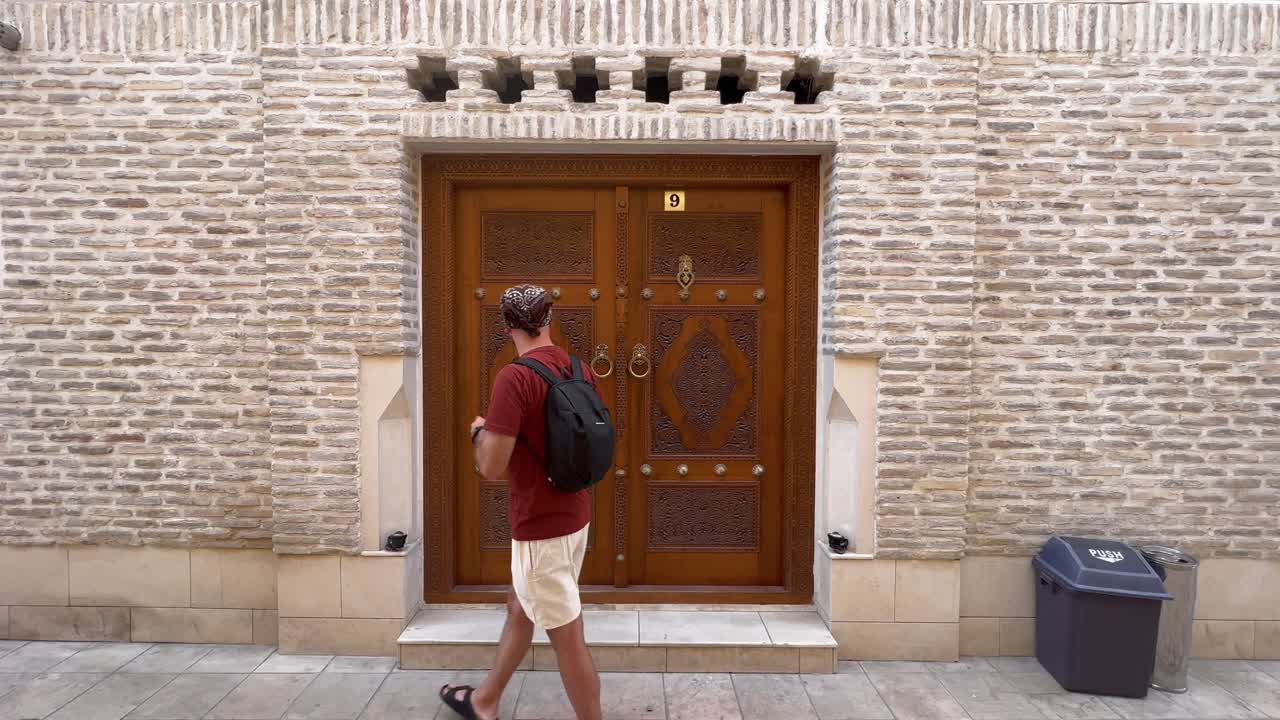 paso en la historia: vista estática de 4k de un joven que emerge de una puerta de madera tradicional en la histórica ciudad vieja de bukhara, uzbekistán