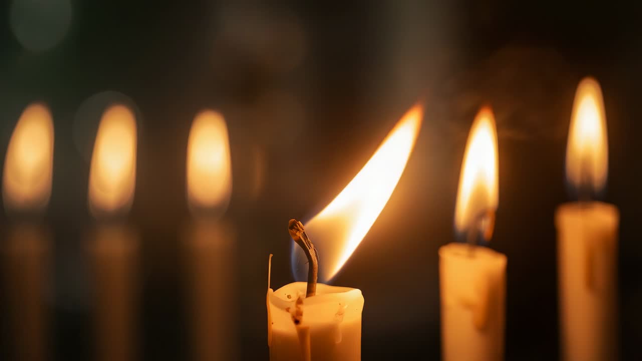 Flickering wax candle responding to breeze above melting wax in dim space, with blurred candles