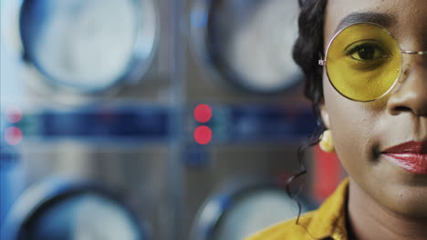 close up of half face of young pretty stylish woman with red lips and in yellow glasses smiling to camera in laundry service room