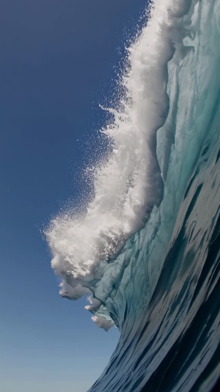 Scatto dinamico dal basso di un'onda oceanica che si infrange su un cielo limpido, catturando potenza e bellezza