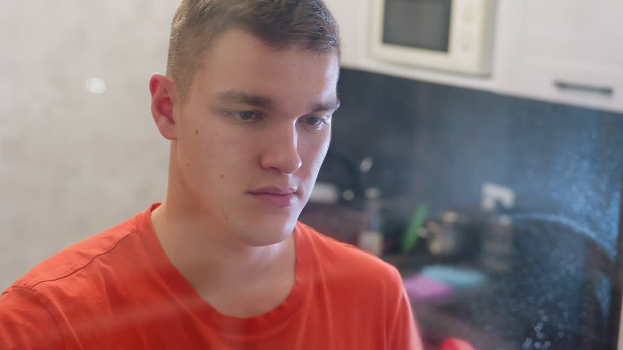 Adult in orange shirt spraying mirror with cleaning solution and wiping surface using green towel, carefully removing water streaks and spray marks while focusing on hygiene