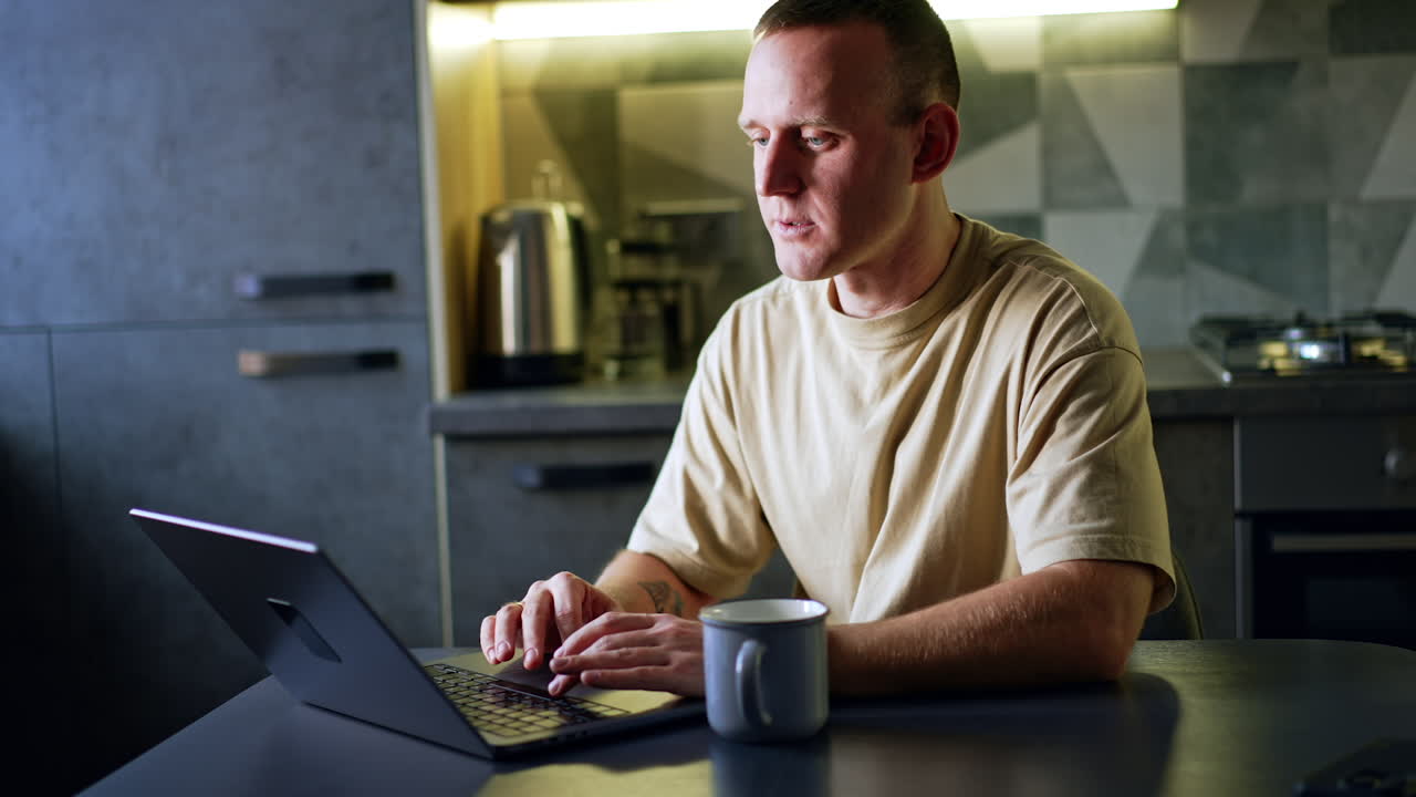 Caucasian man work at laptop sitting in his kitchen. Working freelance remote from home.