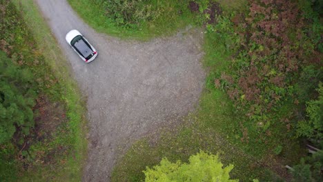 aerial view of a e-car leaving a parking lot, in the forests of switzerland - top down, drone shot