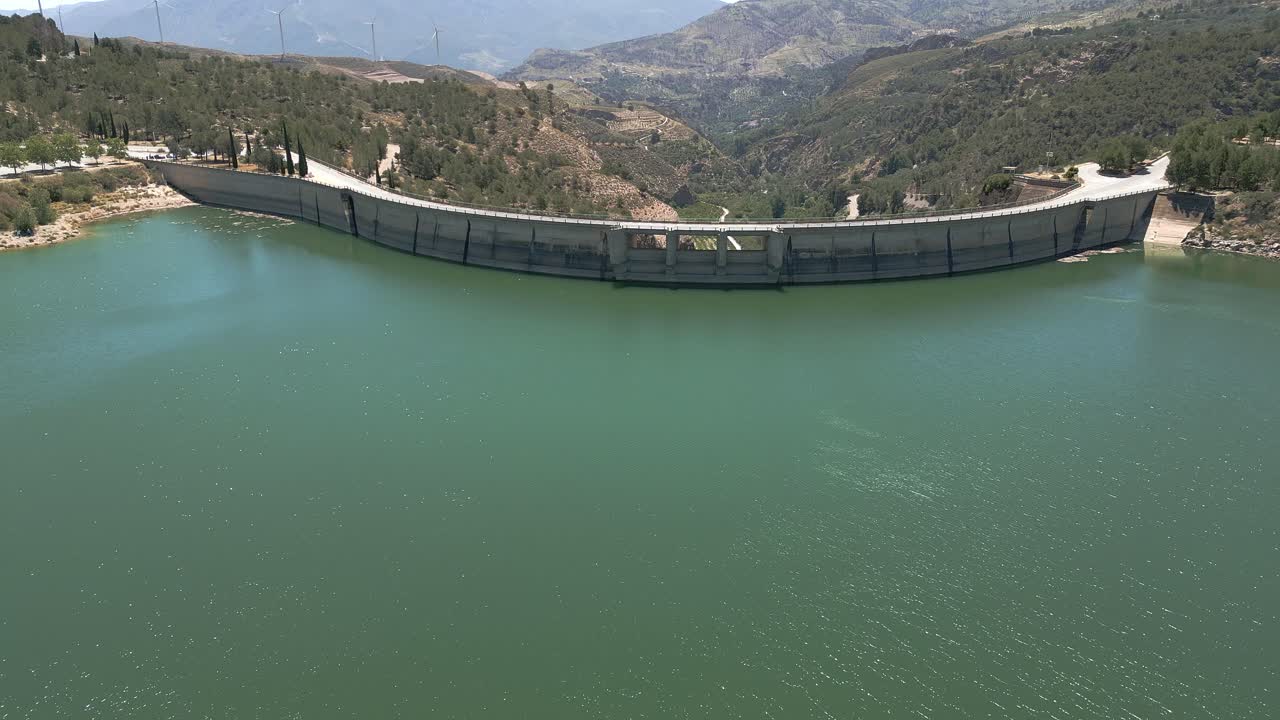 Vault dam. Panoramic aerial view in ascend of road over curved dam. Spain.