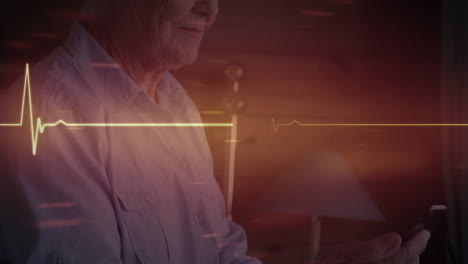 monitor de frecuencia cardíaca rojo brillante contra una mujer mayor caucásica que usa un teléfono inteligente en casa