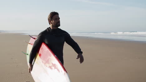 medium shot of a male surfer with artificial leg walking along beach and holding surfboard under arm