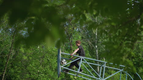 a young boy sits focused on blue iron outdoor equipment, gripping both sides of the iron, as a ball remains stuck in the framework