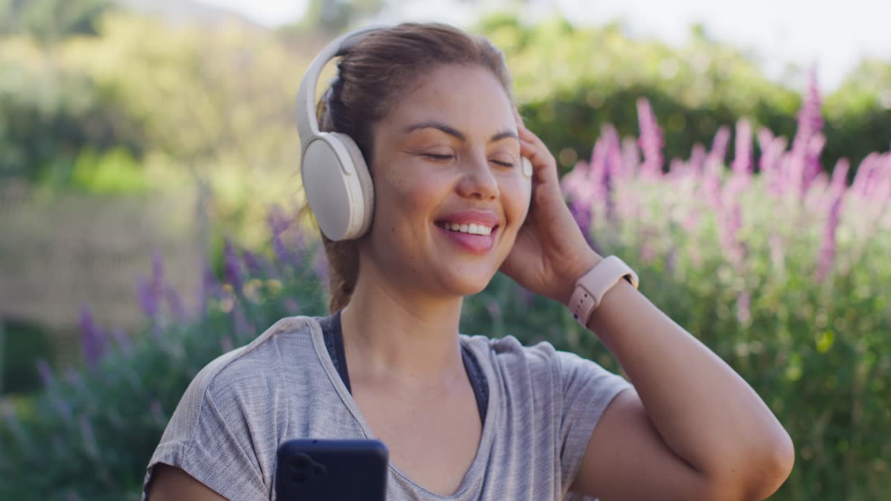 Donna afroamericana adulta che tiene il telefono con le cuffie, ascolta una canzone e si aggiusta al parco
