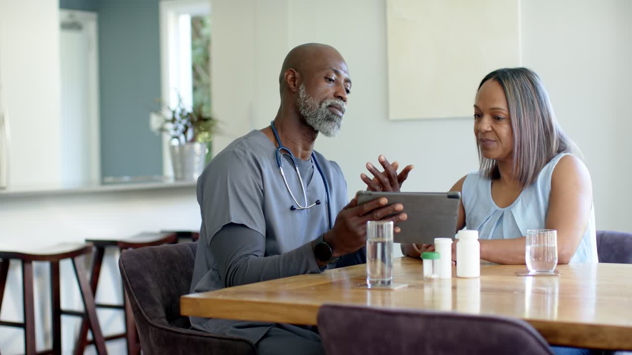 Clinician placing tablet, pointing to pill organizer, bottles, explaining meds to patient at table