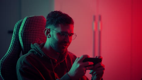 Fröhlicher-Gamer-Typ,-Der-Im-Wettkampf-Videospiele-Online-Mit-Smartphone-Spielt,-Buntes-Neonlicht-Im-Wohnzimmer-Nachts-In-Einem-Modernen-Haus.-E-Sport-Streaming-Spiel,-Online-Aktivität-In-Quarantäne-Zu-Hause.-Hochwertiges-4K-Filmmaterial