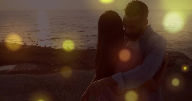 Coppia che si abbraccia in riva all'oceano, circondata da luci luminose in un'animazione romantica.