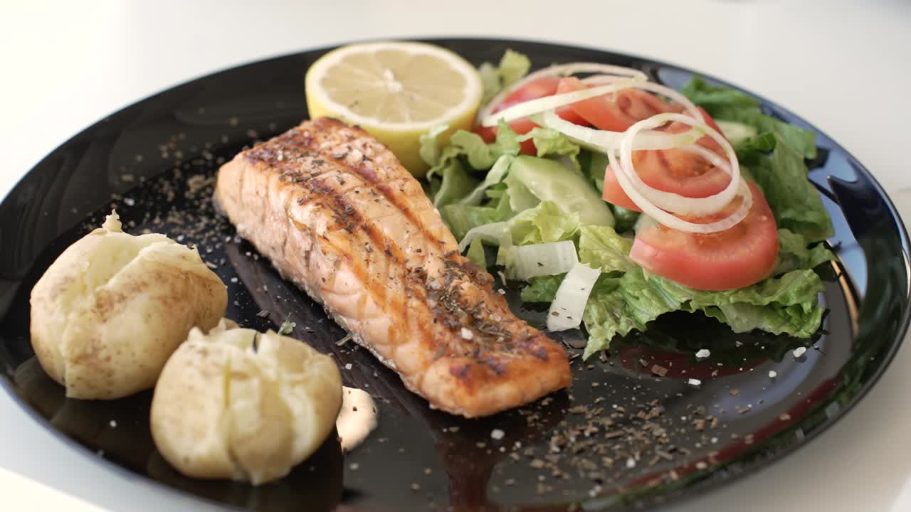 Tasty grilled salmon with fresh salad and lemon served on a modern black plate