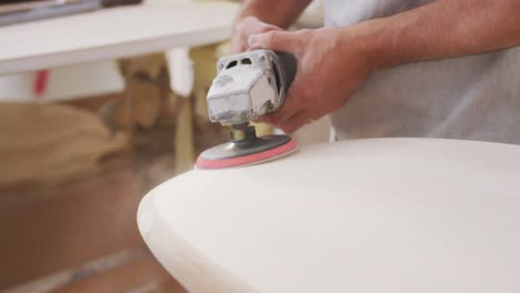 caucasian male surfboard maker wearing a breathing face mask and shaping a wooden surfboard