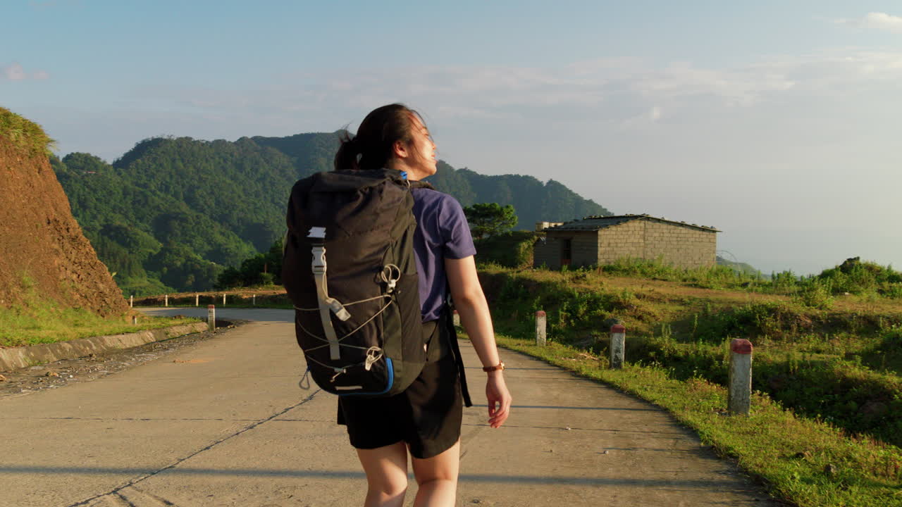 movimiento lento de una viajera sola con mochila caminando por el campo rural durante un día soleado con vista panorámica de las montañas