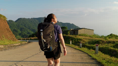 Zeitlupe-Einer-Alleinreisenden-Mit-Rucksack,-Die-An-Einem-Sonnigen-Tag-Mit-Panoramablick-Auf-Die-Berge-Auf-Dem-Land-Spaziert