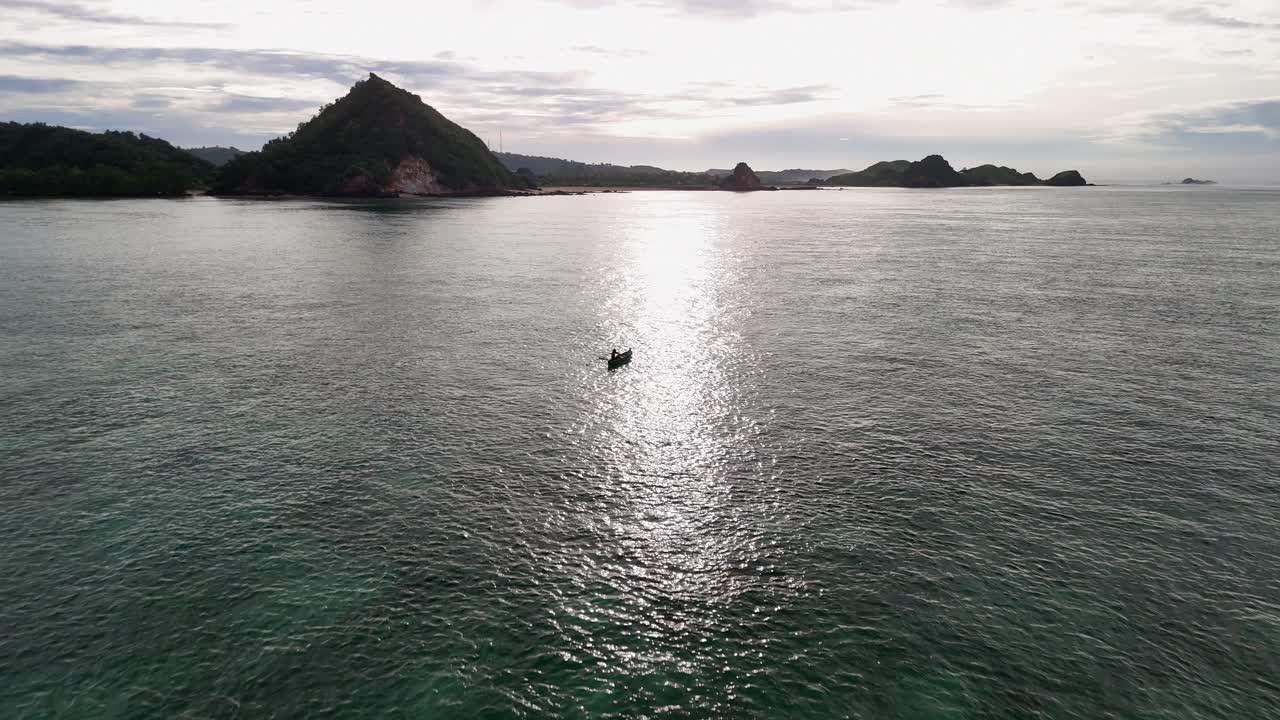 Flyover of lone fisherman in outrigger canoe in sun beam on Lombok sea