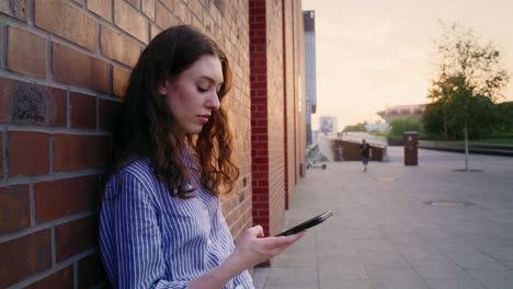 Female-caucasian-student-standing-with-book-and-browsing-mobile-phone