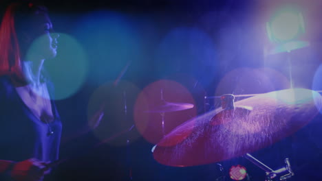 female drummer on live music stage playing drum kit under colored lights, with animated sound waves
