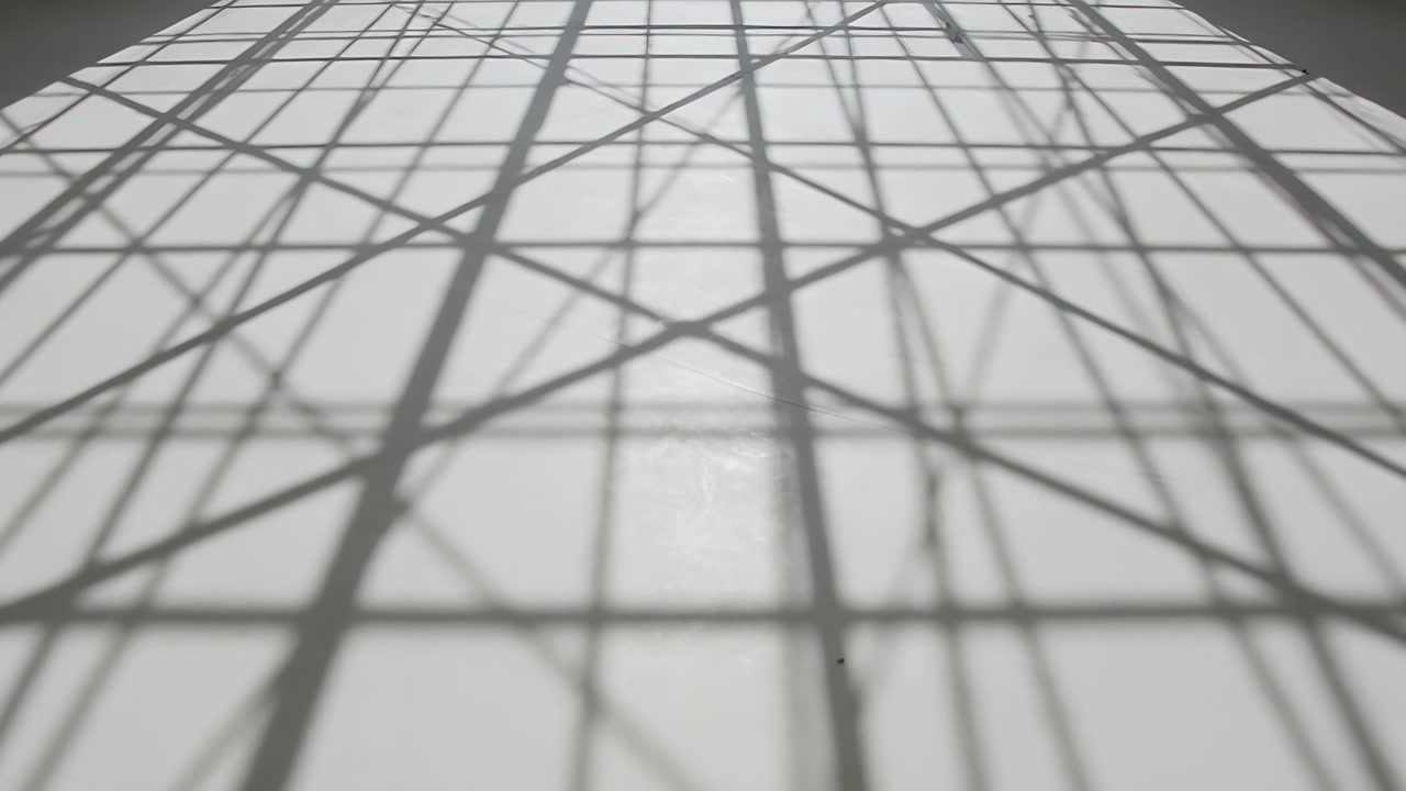 Telecamera in movimento che rivela una griglia d'ombra con linee diagonali più sottili che convergono su una superficie chiara, con una finestra.