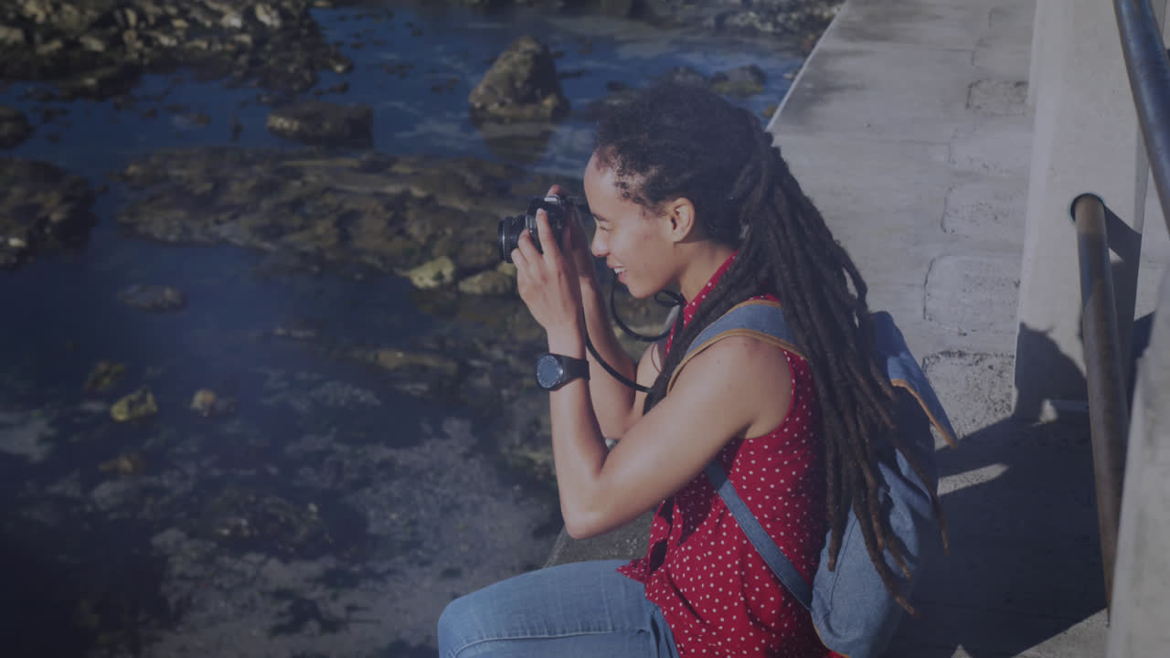 animación de puntos de luz sobre mujer biracial tomando fotos con cámara en el paseo marítimo