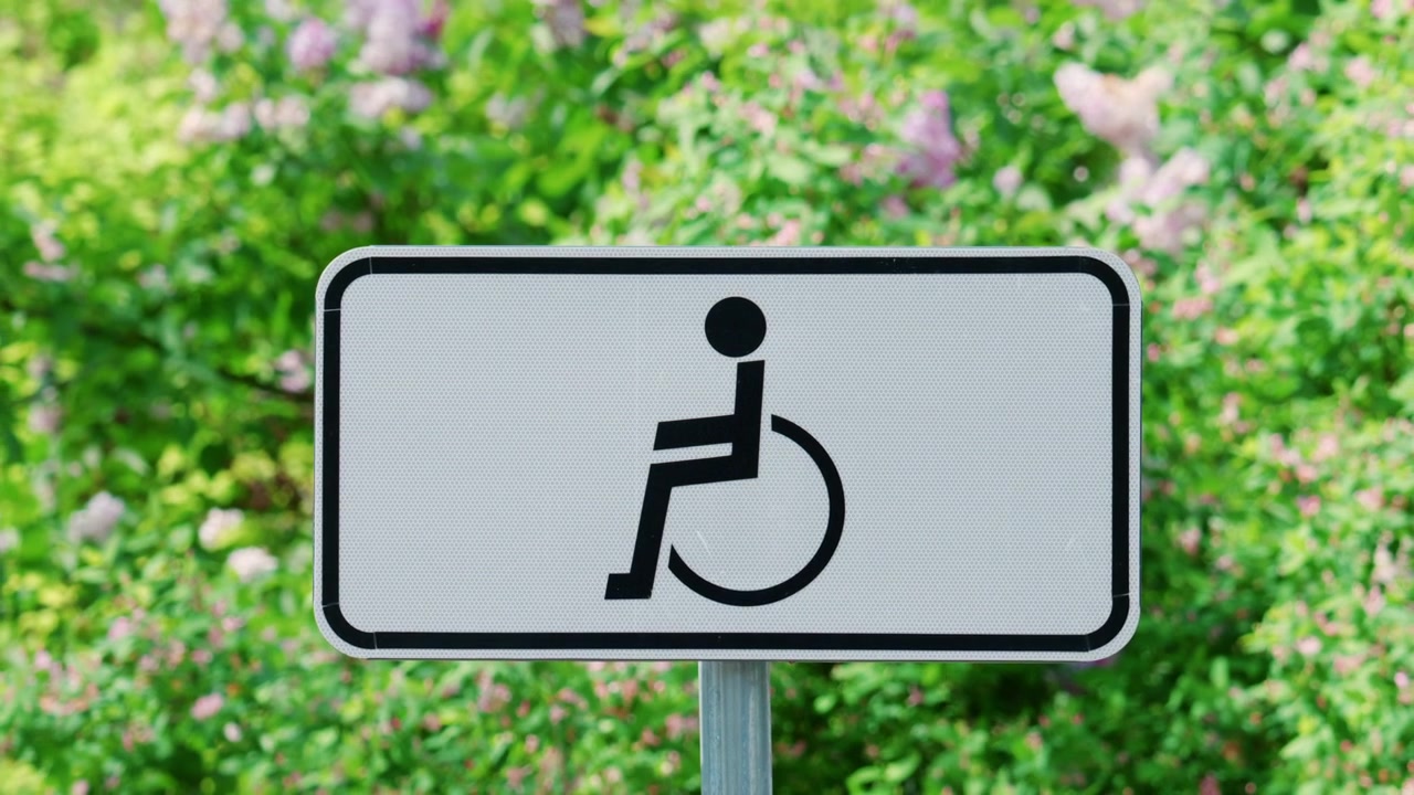 Wheelchair accessibility sign displayed outdoors against a background of green plants and flowers