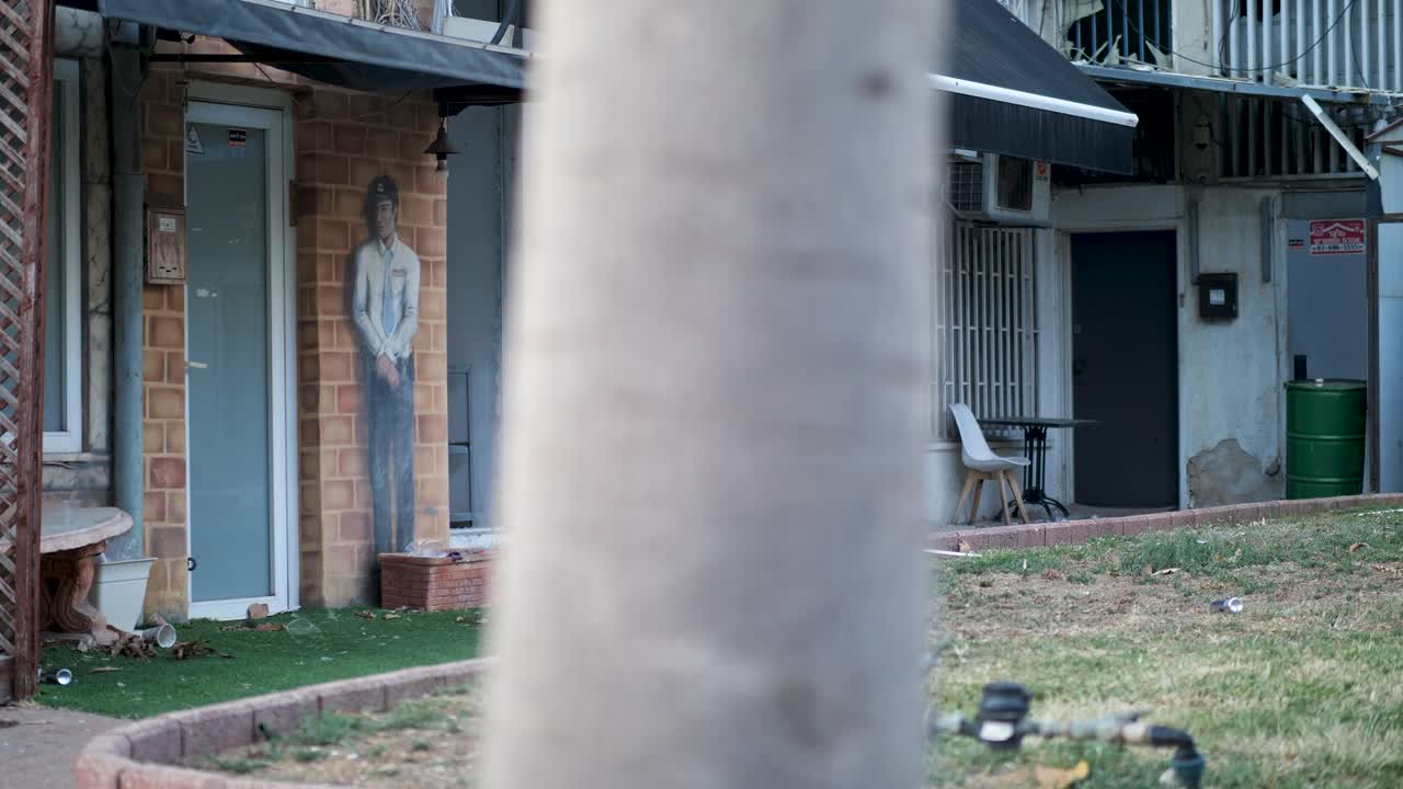 Street-level view of damaged shops in Ramat Gan, Tel Aviv, showing shattered glass and mural of a man after an Iranian missile strike.