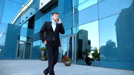 young businessman talking on phone near office and celebrating achievement. business man heard good news on cellphone and having positive emotions. portrait of guy is happy with success. slow motion