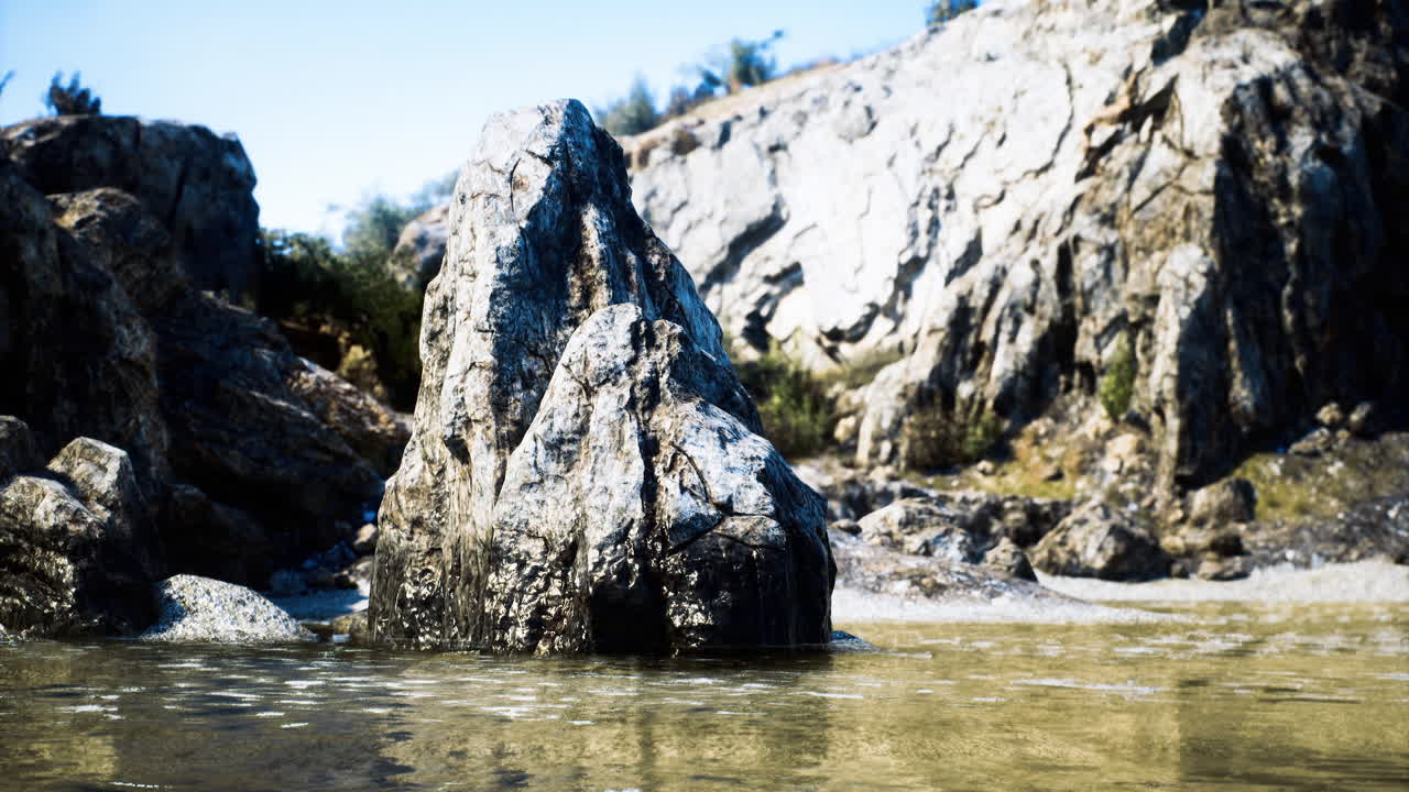 Large rock formation near calm water surrounded by cliffs and trees