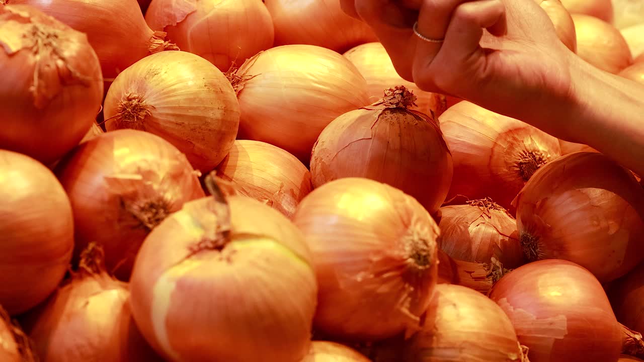 Hands choose yellow onions from a vibrant supermarket display under warm lighting, capturing a moment of grocery shopping