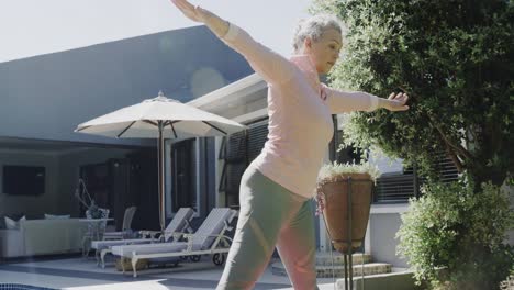 Happy-senior-caucasian-woman-doing-yoga,-stretching-in-sunny-garden,-slow-motion