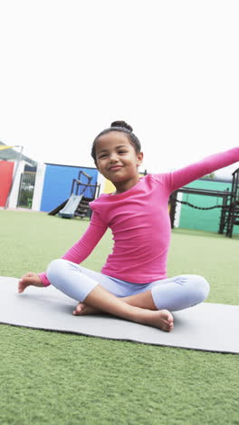 vertical video: in a schoolyard, a young biracial girl practices yoga