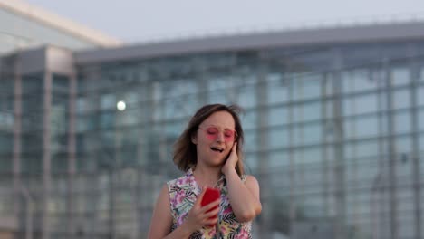 Turista-Feliz-Con-Gafas-De-Sol-De-Moda-Bailando-Y-Escuchando-Música-Con-Auriculares-Usando-Un-Teléfono-Inteligente