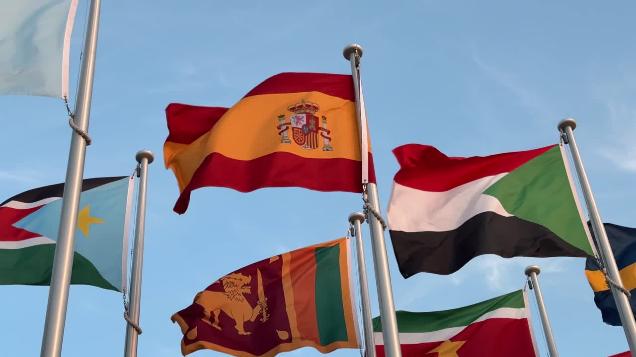 A low-angle shot of many colorful flags waving in the wind, with the Spanish flag prominent in the center, symbolizing national pride and global unity on a bright sunny day