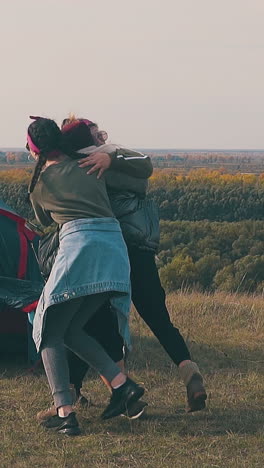 pudgy lady runs to girl friends and hugs by blue camp tent against calm river with forests on opposite bank slow motion