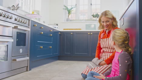 Grandmother-And-Granddaughter-Waiting-For-Cupcakes-To-Bake-In-Kitchen-At-Home