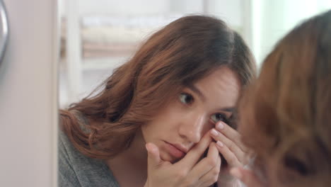 Young-woman-putting-contact-lens-for-eye-front-bathroom-mirror-in-home