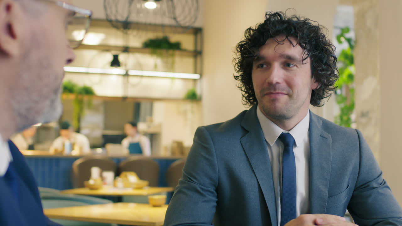 Businessman Speaking and Shaking Hands with Senior Executive in Cafe