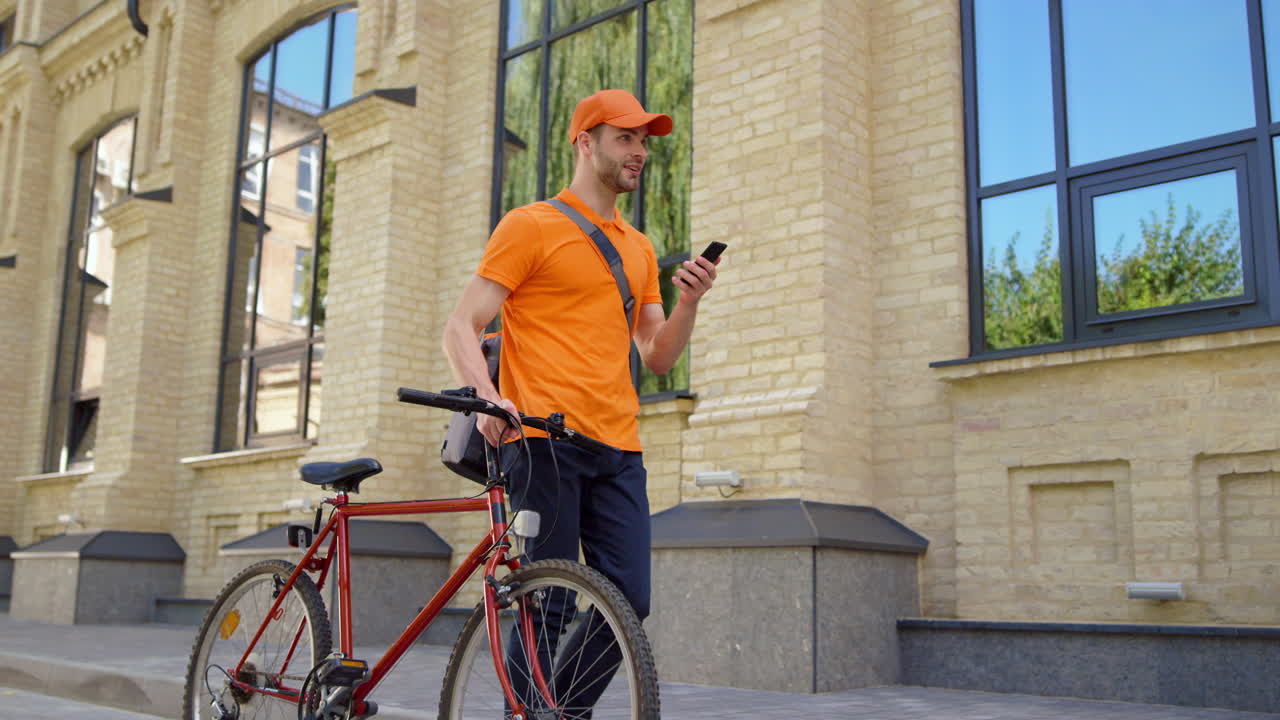 Smiling courier using mobile phone outdoors. Man delivering food with bike.